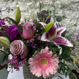 Pink and purple mixed bouquet with lilies, roses, and a gerbera daisy in a glass vase
