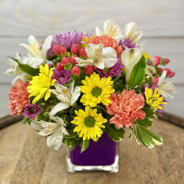 Colorful mixed bouquet in a purple vase with daisies, carnations, and white lilies