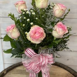 Pink and white roses arranged in a glass vase with a striped ribbon