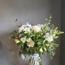 White roses and mixed white flowers in a glass vase with a ribbon