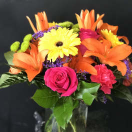 Bright mixed bouquet with orange lilies, pink roses, and yellow daisies in a glass vase