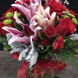 Red roses and pink lilies in a glass vase with a red ribbon