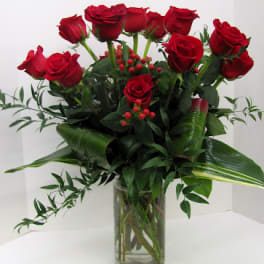 Red roses arranged in a clear glass vase with greenery