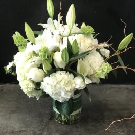 White lilies and hydrangeas in a glass vase with curly branches