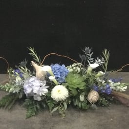Low floral arrangement with blue hydrangeas, white calla lilies, and succulents
