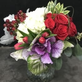 Bouquet of red roses, white hydrangea, and purple flowers in a glass vase