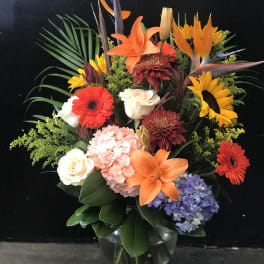 Mixed bouquet with orange lilies, sunflowers, roses, and hydrangea in a glass vase