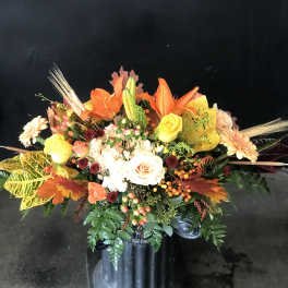 Autumn floral arrangement with roses, lilies, and daisies in a black vase