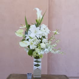 Tall white floral arrangement in a wrapped vase against a pink wall