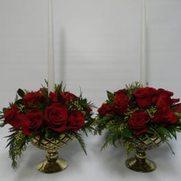 Two red rose arrangements in gold pedestal bowls with tall white candles