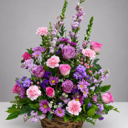 Pink and purple mixed flower arrangement in a wicker basket