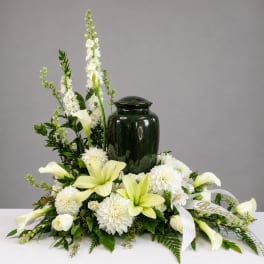 White lilies and mums arranged around a dark green urn