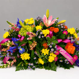 Colorful floral spray with lilies, roses, and ribbon on a low base