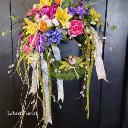 Colorful floral wreath with lilies, roses, and ribbons on a dark door