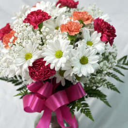 Bouquet of white daisies and pink carnations with a magenta ribbon in a vase