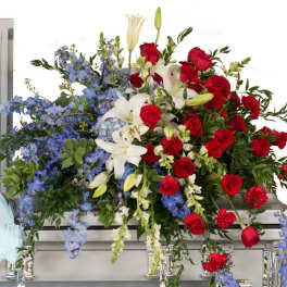 Large floral casket spray with red roses, white lilies, and blue flowers