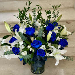 Blue roses and white lilies in a glass vase with greenery