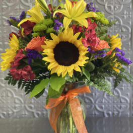 Bouquet of sunflowers, lilies, roses, and purple filler in a glass vase