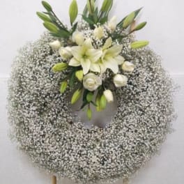 Large white wreath of baby's breath with white lilies and roses on a stand