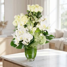White roses and orchids arranged in a green glass vase