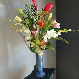 Tall tropical flower arrangement in a blue glass vase with pink, white, and red blooms