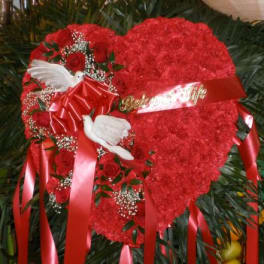 Heart-shaped red floral tribute with roses, ribbons, and white doves