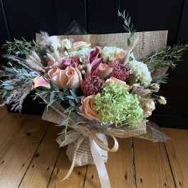 Bouquet of peach roses, hydrangeas, and dried grasses wrapped in newspaper