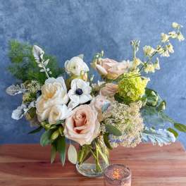 Blush and white bouquet in a clear glass vase with a small candle nearby