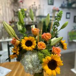 Bouquet of sunflowers, orange roses, lilies, and white hydrangea in a glass vase