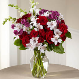 Bouquet of red roses, white alstroemeria, and purple carnations in a glass vase