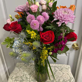 Mixed bouquet of red roses, pink blooms, and lavender flowers in a glass vase