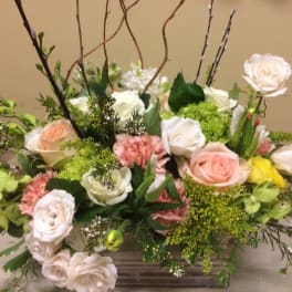 Mixed bouquet of roses, carnations, and green blooms in a low rectangular container