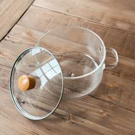 Clear glass pot with lid and wooden knob on a wooden table