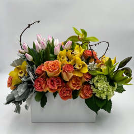 Mixed floral arrangement in a white rectangular vase with roses, orchids, and tulips