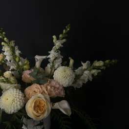 Soft peach and white flowers arranged in a white vase against a dark background.