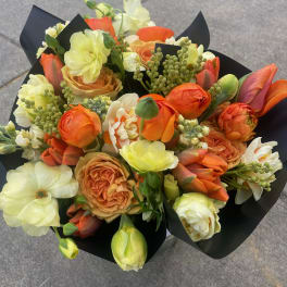 Bouquet of orange, cream, and pale yellow flowers wrapped in black paper