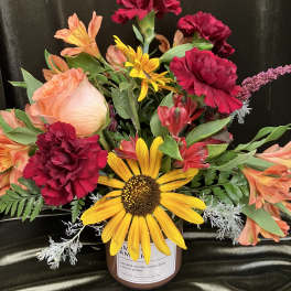 Mixed bouquet with a sunflower, carnations, and alstroemeria in a candle jar