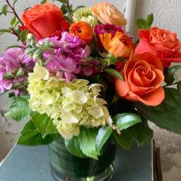 Mixed bouquet of orange roses, hydrangeas, and pink flowers in a glass vase