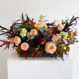 Peach roses and pale yellow flowers in a low rectangular arrangement