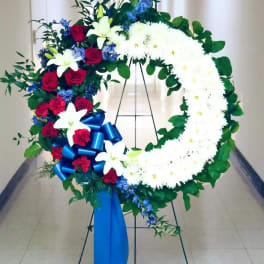 Large floral wreath with white chrysanthemums, red roses, blue flowers, and a blue ribbon