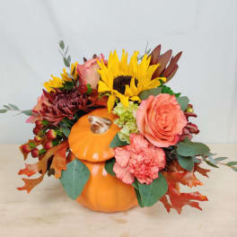 Fall floral arrangement in an orange pumpkin container with sunflowers and roses