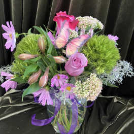 Pink and lavender floral arrangement in a glass vase with a butterfly accent