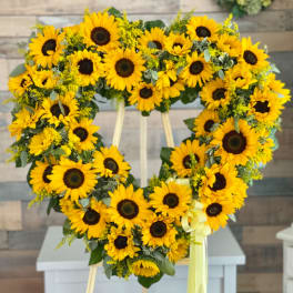 Heart-shaped sunflower wreath on a stand with a yellow ribbon