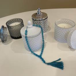 Decorative glass candles and lidded jars on a table, with a blue bead strand draped over one jar.