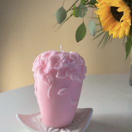 Pink floral candle on a white dish, with a sunflower arrangement in the background