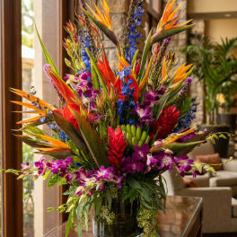 Tropical flower arrangement with purple orchids and orange bird-of-paradise in a glass vase