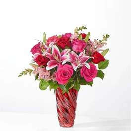 Pink and red roses with lilies in a red glass vase