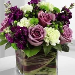Purple roses and white-green blooms arranged in a square glass vase