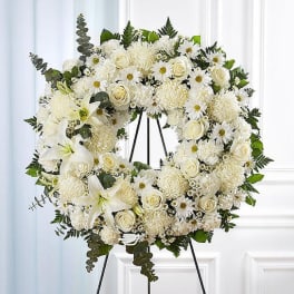 White floral wreath on a black stand with roses and daisies