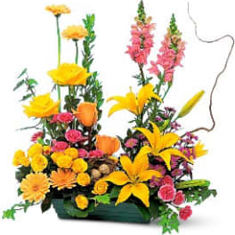 Bright arrangement of yellow lilies, orange roses, and pink flowers in a low green container